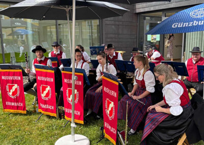 Der Musikverein Krumbach sitzt unter Sonnenschirmen beim Tag der offenen Tür vorm Therapiepavillon