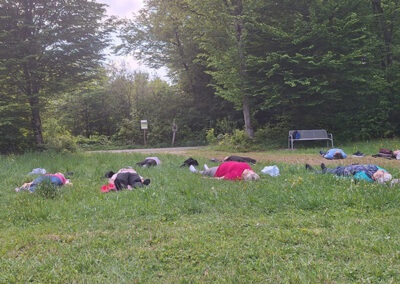 Die Teilnehmer der Yogawanderung liegen entspannt auf ihren Matten im grünen Gras